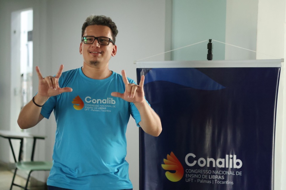 homem fazendo sinais de libras diante de um banner do evento